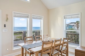 A dining area with a table and chairs, large windows with ocean views, and a balcony with a railing. - Arenita & Playita 3 Bedroom Home (Port Bolivar)