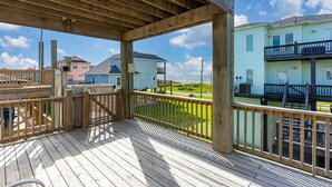 A wooden deck with a view of a residential area, including a two-story building with a balcony. - Arenita & Playita 3 Bedroom Home (Port Bolivar)