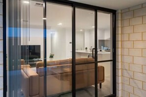 Ein modernes Interieur mit einer Couch, einer Glastrennwand und einem sichtbaren Küchenbereich dahinter.