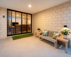 Ein modernes Wohnzimmer mit einer Schiebetür zum Balkon, einer Holzbank, einem kleinen Tisch mit Pflanze und einer Wandleuchte.