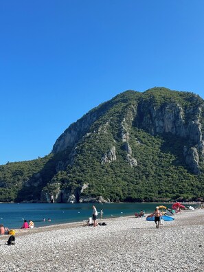 A pebbled beach with people, a mountain, and clear blue sky.