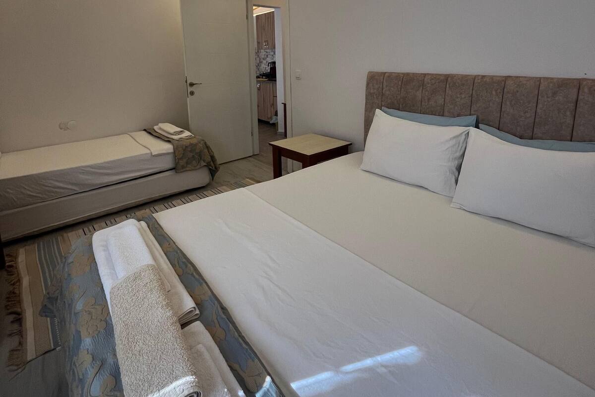 Ein Hotelzimmer mit einem großen Bett, einem kleineren Bett, einem Nachttisch und einem durchgegangene Tür erkennbaren Badezimmer.