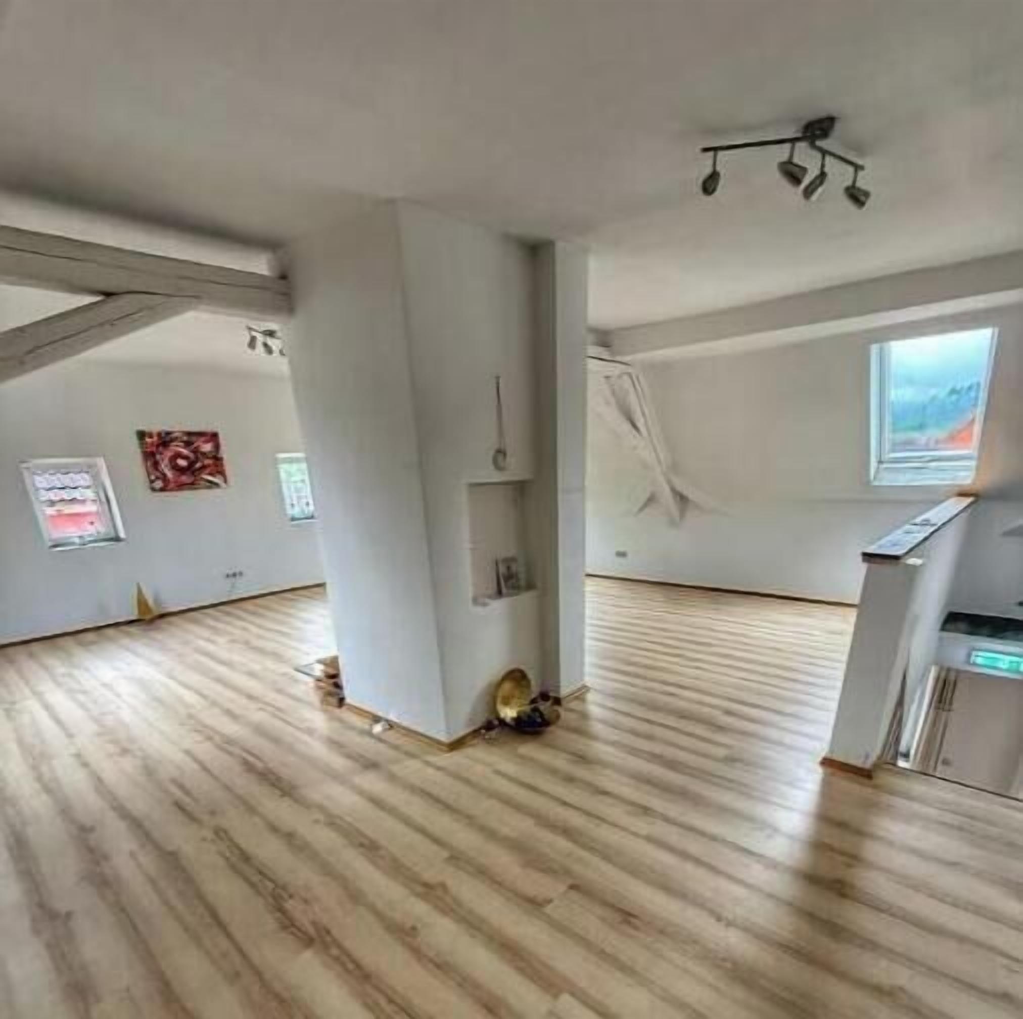 Um quarto vazio com soalho de madeira, um candeeiro no teto e uma janela com vista.