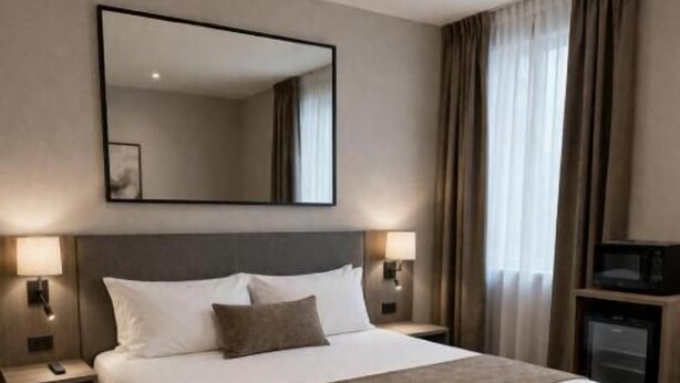 A hotel room with a large bed, bedside lamps, a flat-screen TV, and a large mirror on the wall. - Hôtel Le Castanea (Roannes-Saint-Mary)