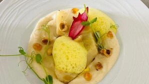 A white plate with a food dish, garnished with herbs and a red leaf. - Hôtel Le Castanea (Roannes-Saint-Mary)
