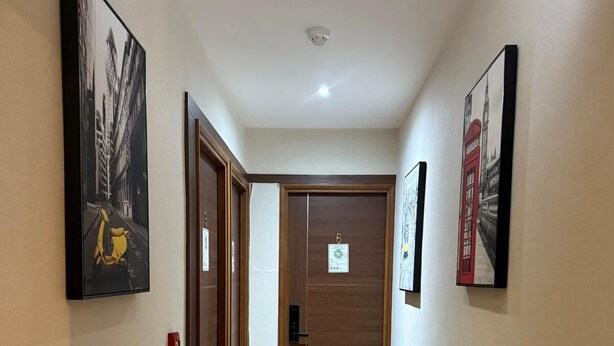 Un pasillo con una puerta de madera marcada con el número 6, un detector de incendios y cuadros en las paredes.