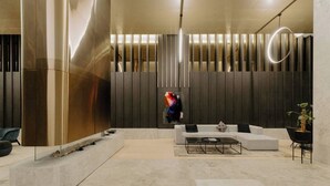 A modern lobby with a curved reception desk, a seating area with a sofa and coffee table, and a decorative wall with vertical panels. - Puddings Designer 2B2B WSP | CBD Southern Cross (Melbourne)