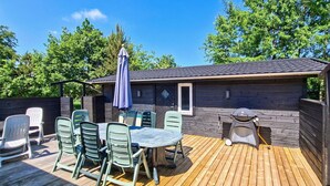 Eine Terrasse im Freien mit Tisch und Stühlen, einem Grill und einem überdachten Bereich ebenfalls mit Tisch und Stühlen.