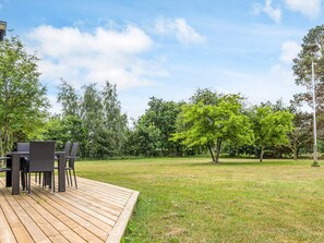 Eine Holzterrasse mit Gartenmöbeln, umgeben von einer Rasenfläche und Bäumen.