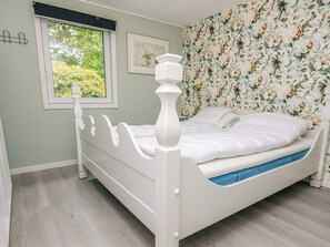 Un dormitorio con una cama con dosel blanca, una ventana con vistas a zonas verdes y papel tapiz floral.