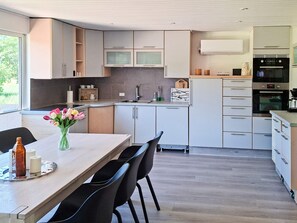 A modern kitchen with white cabinets, a wooden dining table, and black chairs. - 4 Star Holiday Home in Hals (Hals)