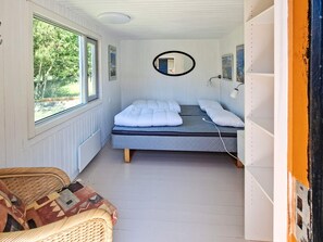 Ein kleines Zimmer mit zwei Betten, einem Korbstuhl, einem Spiegel und Blick ins Grüne.