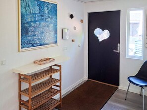 Un pasillo con un estante de madera, una puerta negra con un corte en forma de corazón, un cuadro enmarcado y una ventana.