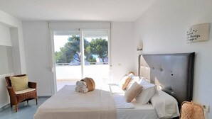 Ein Schlafzimmer mit einem Bett, einem Sessel, einem Nachttisch und Blick durch eine Tür.