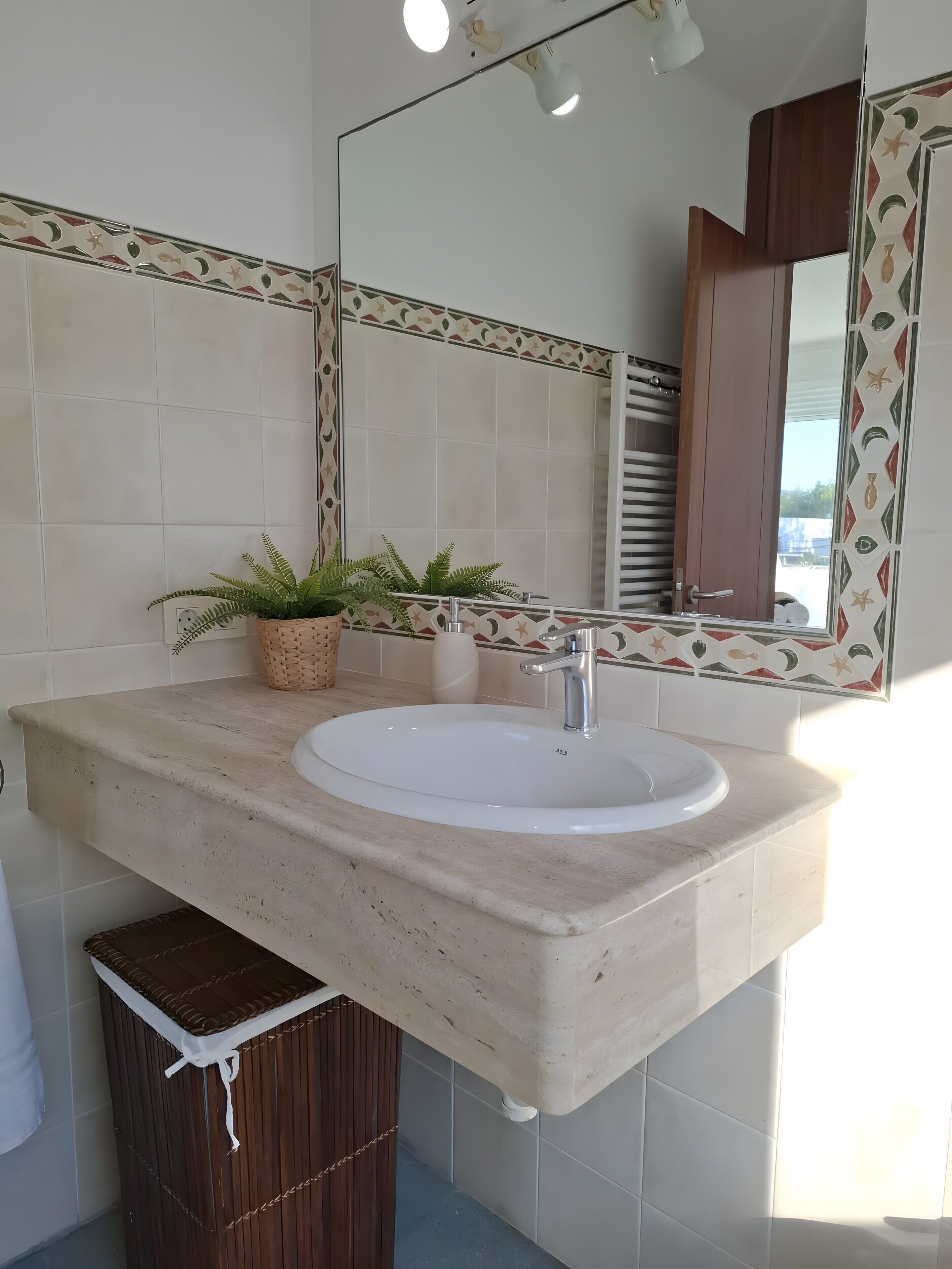 Un baño con lavamanos blanco, espejo y planta en maceta.