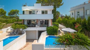 Ein modernes, zweistöckiges Haus mit Swimmingpool, Sitzgelegenheiten im Freien und einem Balkon.