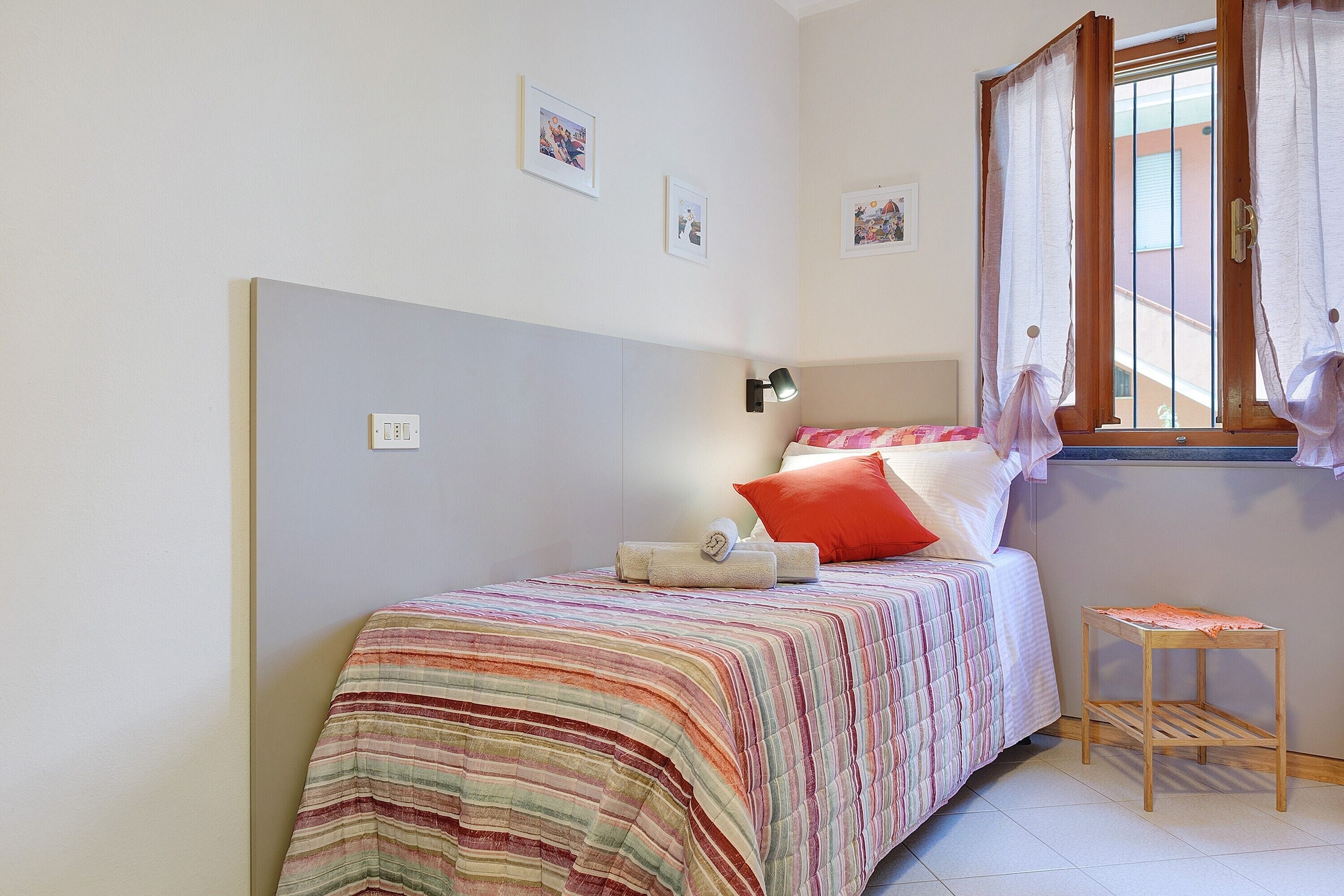 Ein Schlafzimmer mit einem Bett, einem Nachttisch, einer Lampe und einem Fenster mit Vorhängen.
