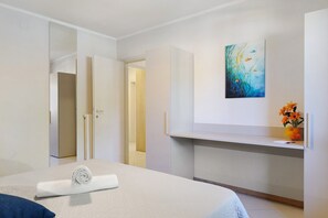 A hotel room with a bed, a desk, a painting, and a vase with flowers.