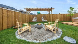 A backyard with a fire pit, two Adirondack chairs, a pergola, and a wooden deck. - The Triple Nest - Where Your Summer Story Begins (Hamilton)