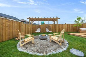 Un jardin avec un foyer, deux fauteuils Adirondack, une pergola et une terrasse en bois.