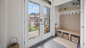 A hallway with a glass door leading outside, a bench with baskets, and a shelf with decorative items. - The Triple Nest - Where Your Summer Story Begins (Hamilton)