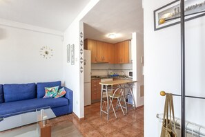 Ein kompakter Wohnraum mit Küchenzeile, einer Couch mit bunten Kissen und einem Essbereich mit kleinem Tisch und Stühlen.
