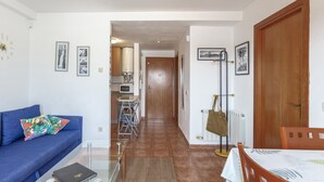 A living room with a blue sofa, a coffee table, and a dining area with a table and chairs. A hallway leads to a kitchen with a microwave and a water heater. - Berni's House Palafolls Apartment with Sea Views, Private Terrace & Air Conditioning (Palafolls)