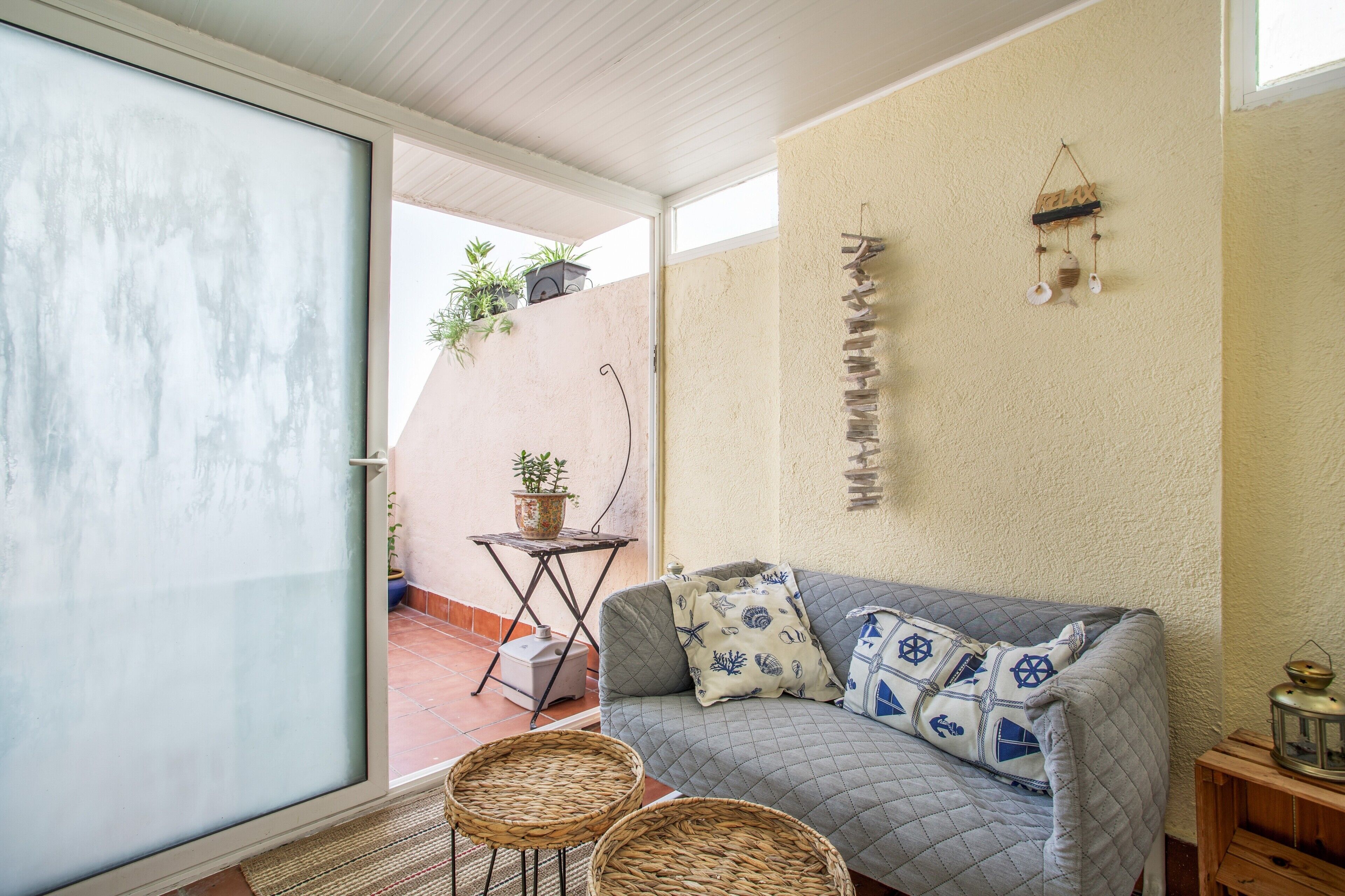 Une pièce chaleureuse avec une porte-fenêtre coulissante donnant sur un patio, un canapé confortable agrémenté de coussins sur le thème de la marine, une petite table avec des plantes en pot et un élément décoratif fixé au mur.