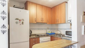 A compact kitchen with wooden cabinets, a built-in oven, a microwave, and a small dining table. - Berni's House Palafolls Apartment with Sea Views, Private Terrace & Air Conditioning (Palafolls)