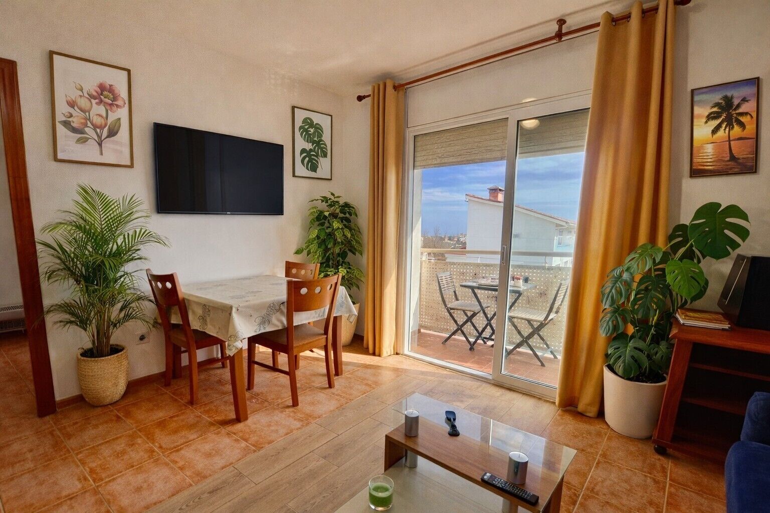 A living room with a dining area, a TV mounted on the wall, and a balcony with a view.