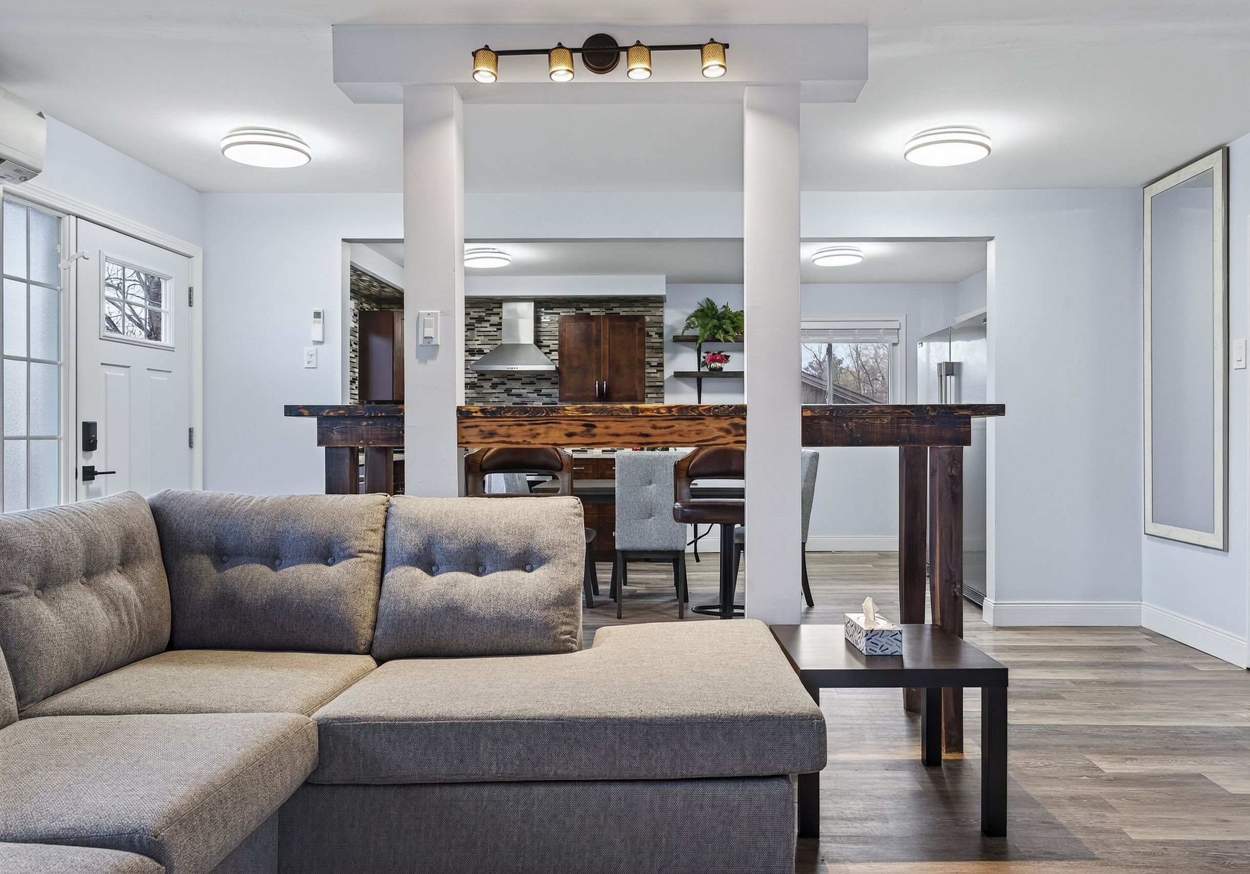 Een moderne woonkamer met een modulaire bank, een eethoek met een houten tafel en stoelen, en een keuken op de achtergrond.