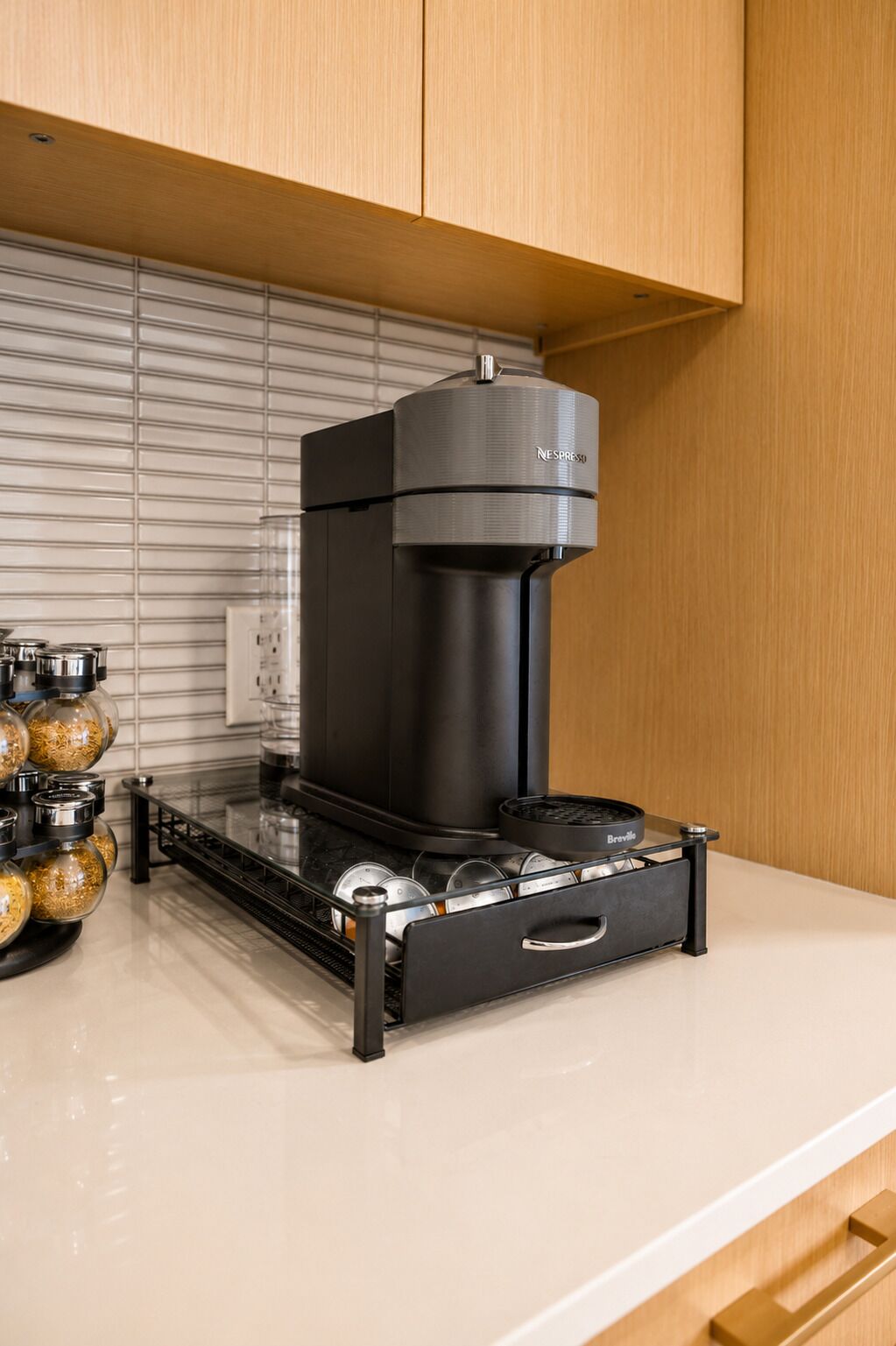 A Nespresso coffee machine on a Breville coffee station in a kitchen with wooden cabinets and a tiled backsplash.