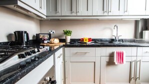 A kitchen with a gas stove, a sink, cabinets, and a countertop with a plant and vegetables. - Luxury St Margarets Flat Richmond Free Parking (Twickenham)