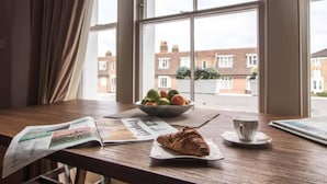 A breakfast table with a croissant, a bowl of fruit, a cup, and a newspaper. - Luxury St Margarets Flat Richmond Free Parking (Twickenham)