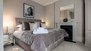 A bedroom with a bed, a bedside table, a lamp, a fireplace, and a mirror. - Luxury St Margarets Flat Richmond Free Parking (Twickenham)
