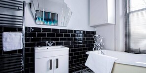 A modern bathroom with a black and white tiled backsplash, a white sink with chrome fixtures, and a bathtub with a chrome faucet. - Luxury St Margarets Flat Richmond Free Parking (Twickenham)