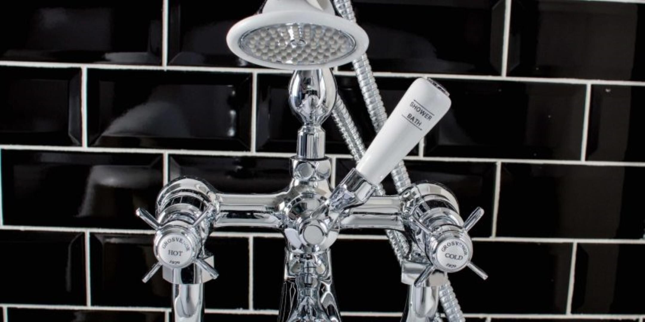 Eine Duschkabine mit verchromten Armaturen, einer Handbrause und zwei Drehgriffen, beschriftet mit 'HEISS' und 'KALT'.