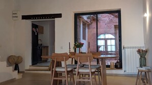 A dining area with wooden chairs and a table, a kitchen in the background, and a view through a large window. - An artist's home in the heart of Roussillon (Roussillon)