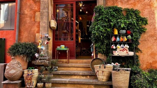 A building with a red door, steps leading up to it, and various items displayed outside, including baskets and pots. - An artist's home in the heart of Roussillon (Roussillon)