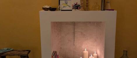 Una chimenea con velas encendidas, una mesa pequeña con libros y un jarrón en la repisa.
