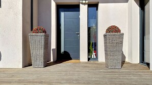 A building entrance with a door, two wicker baskets with flowers, and a wooden deck. - Comfortable villa with pool, AC and garden in Saint‑Paul‑de‑Vence (Saint Paul de Vence)
