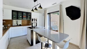 Cozinha moderna com armários brancos, uma ilha central e iluminação pendente.