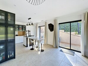 Cozinha moderna com ilha central, área de jantar com mesa e cadeiras, e uma grande porta de vidro deslizante que dá para uma varanda.