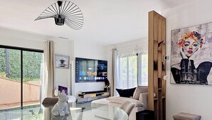A modern living room with a glass dining table, a sofa, a TV, and a painting. - Comfortable villa with pool, AC and garden in Saint‑Paul‑de‑Vence (Saint Paul de Vence)
