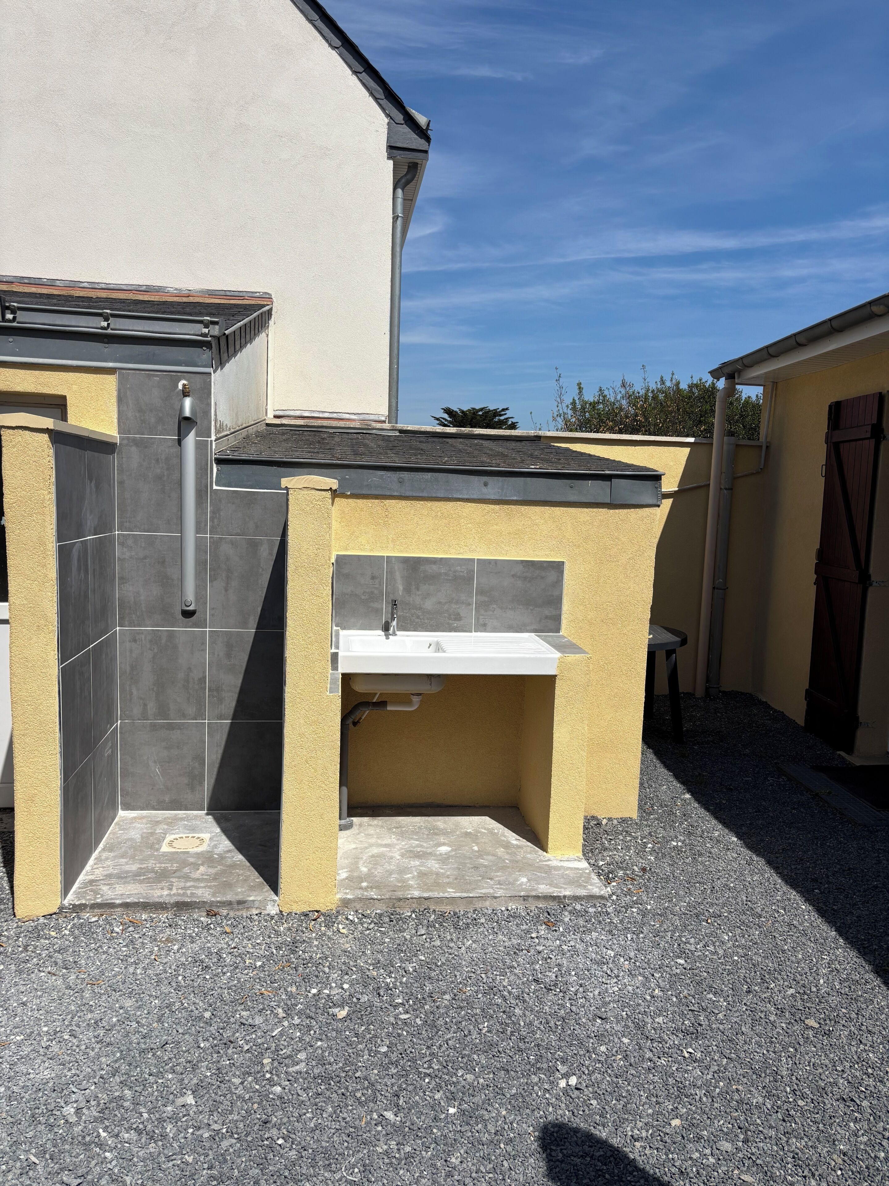 Un petit espace cuisine extérieur doté d’un évier et d’un barbecue intégré, le tout entouré d’un sol en gravier.