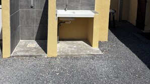 A small outdoor kitchen area with a sink and a built-in barbecue grill, surrounded by a gravel ground.