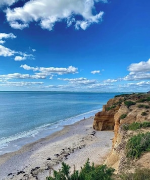 A beach with clear skies, a person walking, and rocky cliffs.