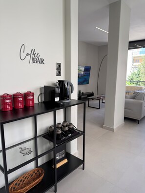 A modern hotel lobby with a coffee bar, a flat-screen TV, and a seating area with a view. - Welcome to Notos Suites - An Athenian Riviera Stay (Voula)