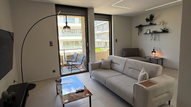 En moderne stue med sofa, sofabord, fjernsyn og en balkon med havemøbler.