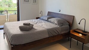 Et moderne soveværelse med seng, natbord og udsigt til grønne omgivelser.